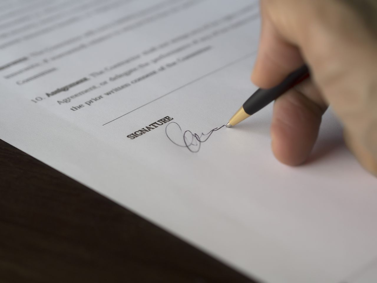 The Art of Drawing Readers In: Your attractive post title goes here A hand signs a formal contract with a pen on a wooden desk.